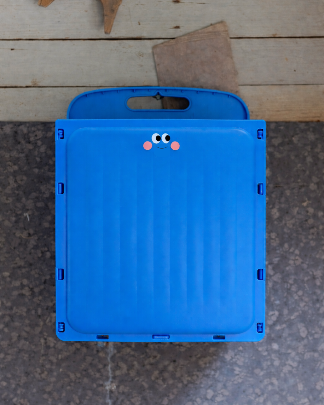 Blue folding stool with cartoon face on a concrete surface